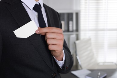 Man taking blank business card from pocket of his jacket in office, closeup. Mockup for design