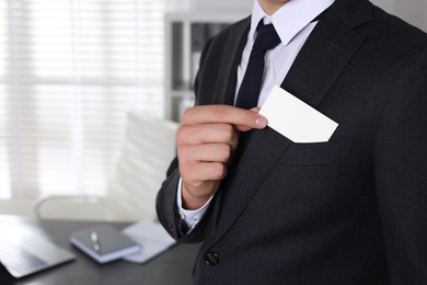 Man taking blank business card from pocket of his jacket in office, closeup. Mockup for design