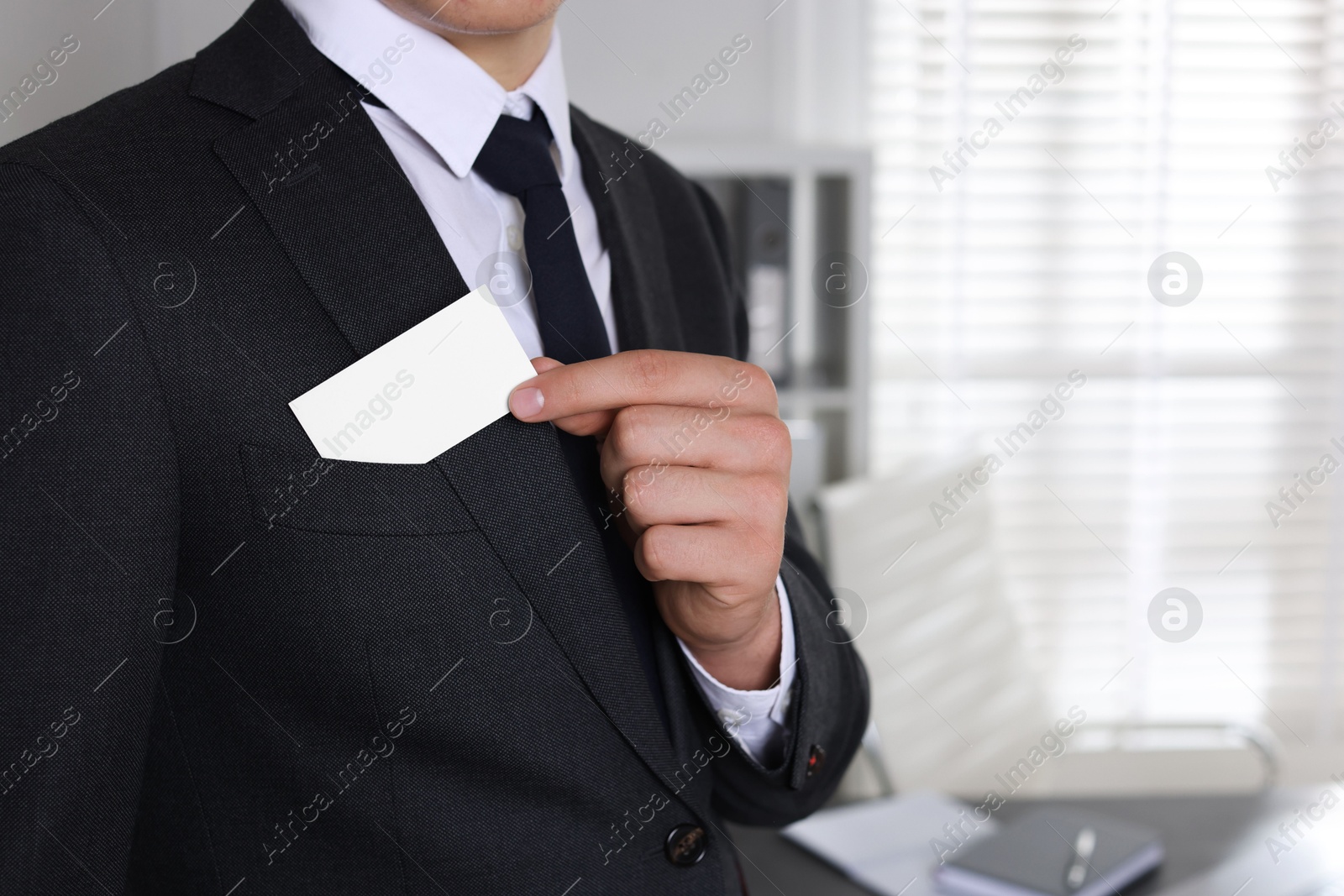 Photo of Man taking blank business card from pocket of his jacket in office, closeup. Mockup for design