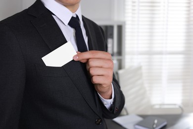 Man taking blank business card from pocket of his jacket in office, closeup. Mockup for design