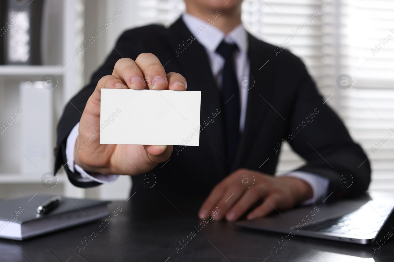 Photo of Man holding blank business card at table in office, closeup. Mockup for design