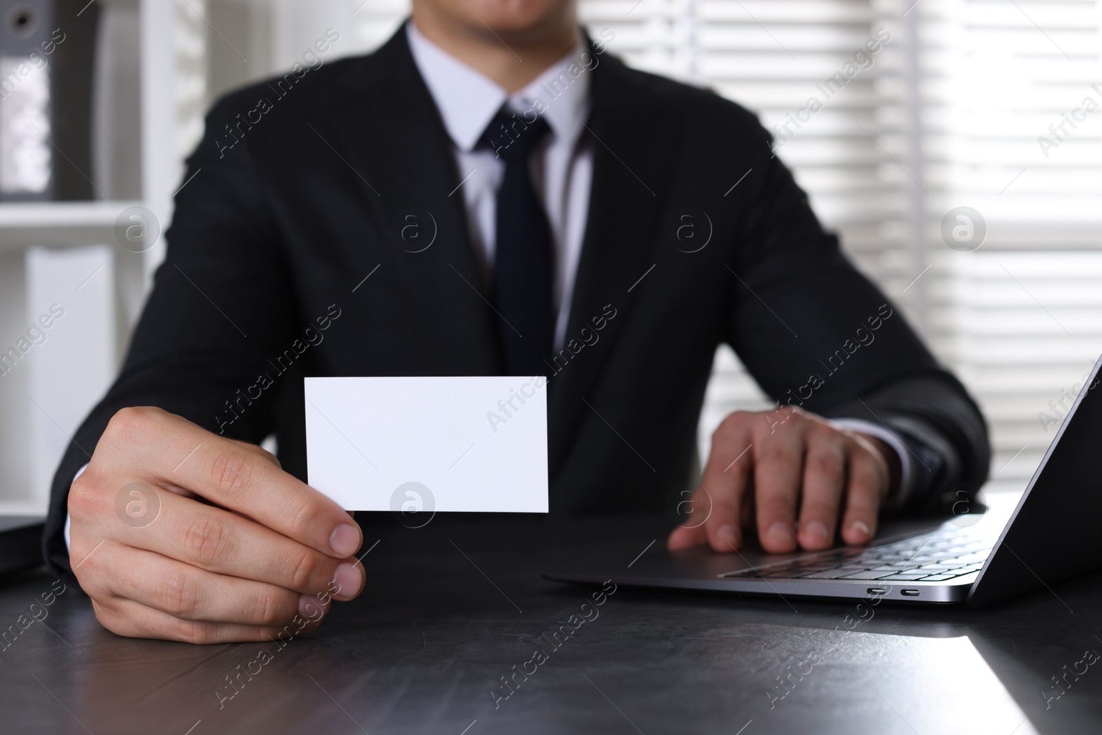 Photo of Man holding blank business card at table in office, closeup. Mockup for design