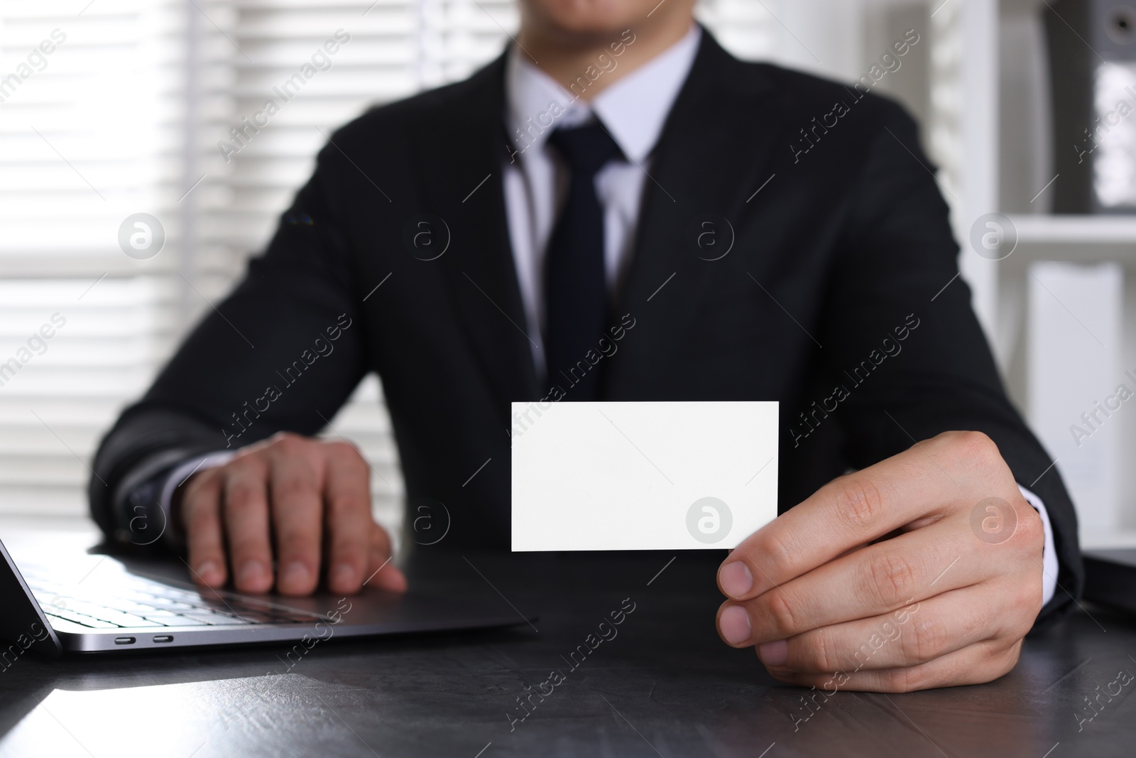 Photo of Man holding blank business card at table in office, closeup. Mockup for design