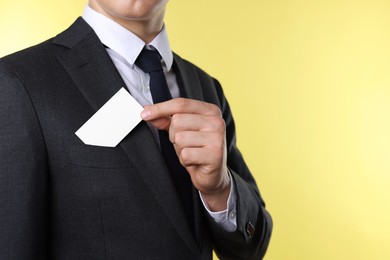 Man taking blank business card from pocket of his jacket on yellow background, closeup. Mockup for design