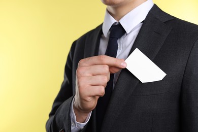 Man taking blank business card from pocket of his jacket on yellow background, closeup. Mockup for design