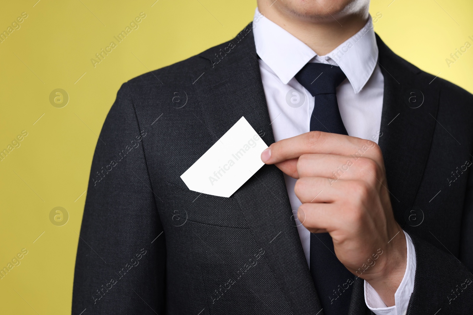 Photo of Man taking blank business card from pocket of his jacket on yellow background, closeup. Mockup for design