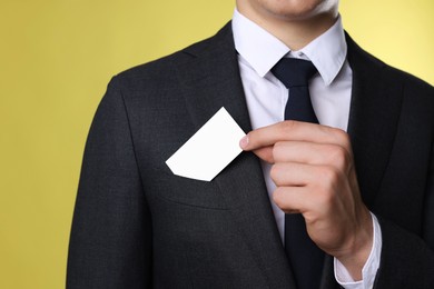 Man taking blank business card from pocket of his jacket on yellow background, closeup. Mockup for design