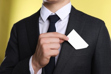 Photo of Man taking blank business card from pocket of his jacket on yellow background, closeup. Mockup for design