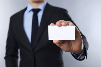 Man holding blank business card on grey background, closeup. Mockup for design