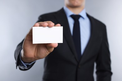 Man holding blank business card on grey background, closeup. Mockup for design