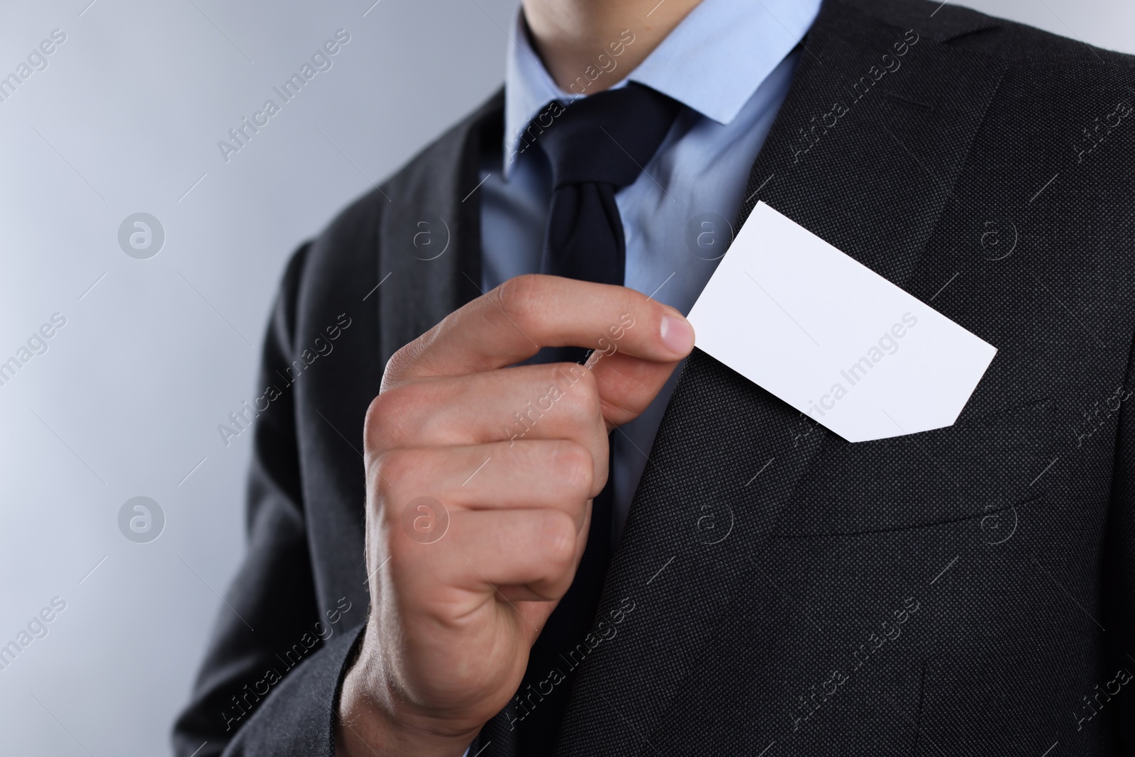 Photo of Man taking blank business card from pocket of his jacket on grey background, closeup. Mockup for design