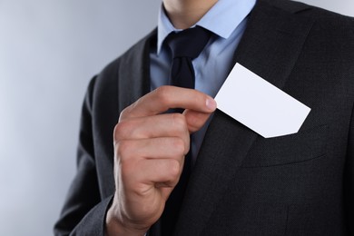 Man taking blank business card from pocket of his jacket on grey background, closeup. Mockup for design