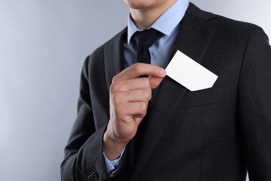 Photo of Man taking blank business card from pocket of his jacket on grey background, closeup. Mockup for design