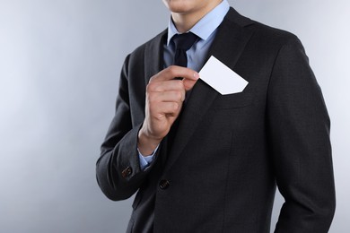 Man taking blank business card from pocket of his jacket on grey background, closeup. Mockup for design