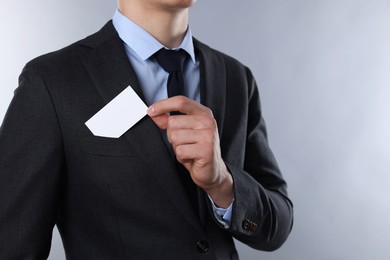 Man taking blank business card from pocket of his jacket on grey background, closeup. Mockup for design