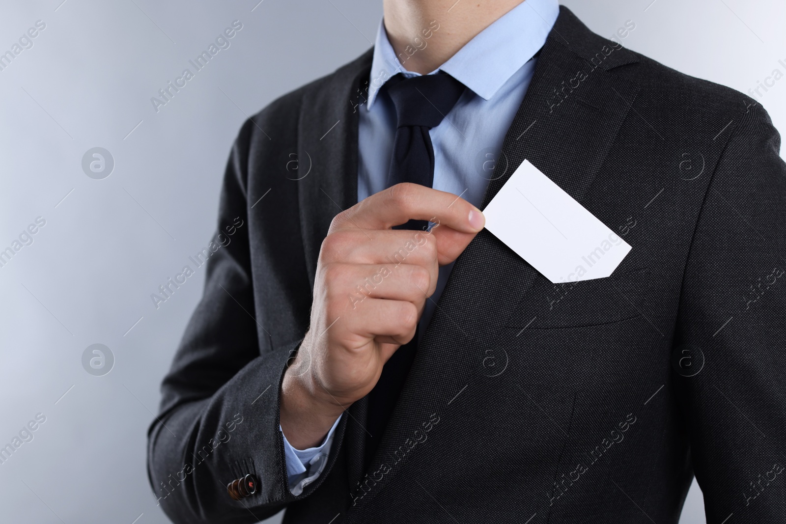 Photo of Man taking blank business card from pocket of his jacket on grey background, closeup. Mockup for design