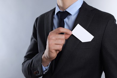 Man taking blank business card from pocket of his jacket on grey background, closeup. Mockup for design