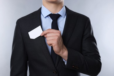 Photo of Man taking blank business card from pocket of his jacket on grey background, closeup. Mockup for design