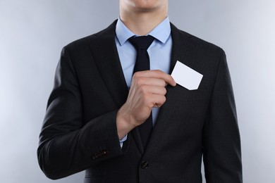 Man taking blank business card from pocket of his jacket on grey background, closeup. Mockup for design