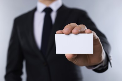 Man holding blank business card on grey background, closeup. Mockup for design