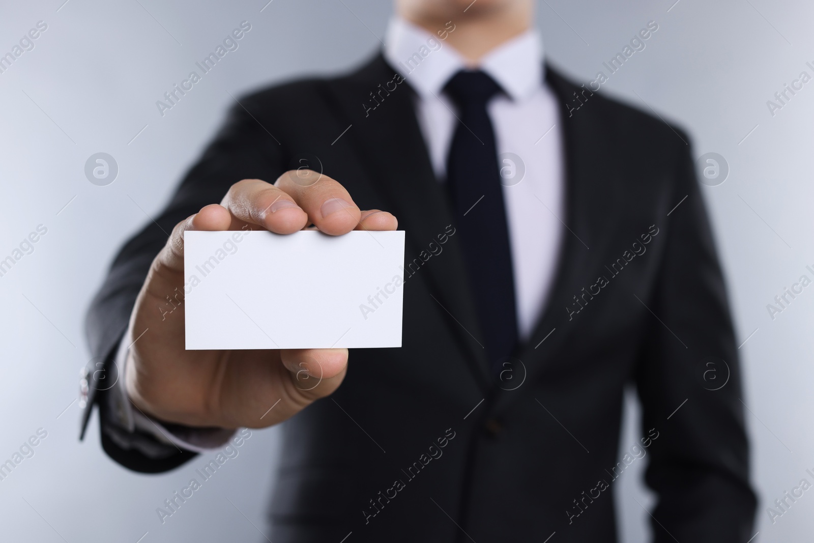 Photo of Man holding blank business card on grey background, closeup. Mockup for design