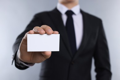 Man holding blank business card on grey background, closeup. Mockup for design