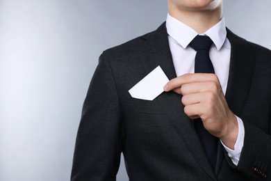 Man taking blank business card from pocket of his jacket on grey background, closeup. Mockup for design