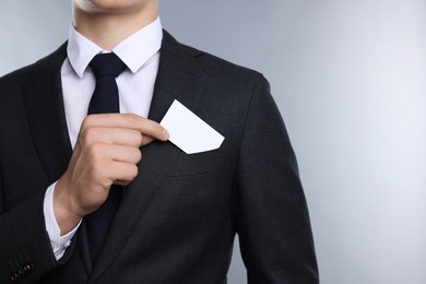 Man taking blank business card from pocket of his jacket on grey background, closeup. Mockup for design