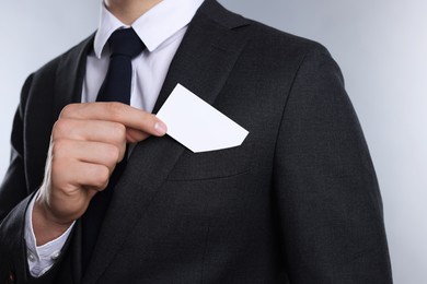 Man taking blank business card from pocket of his jacket on grey background, closeup. Mockup for design