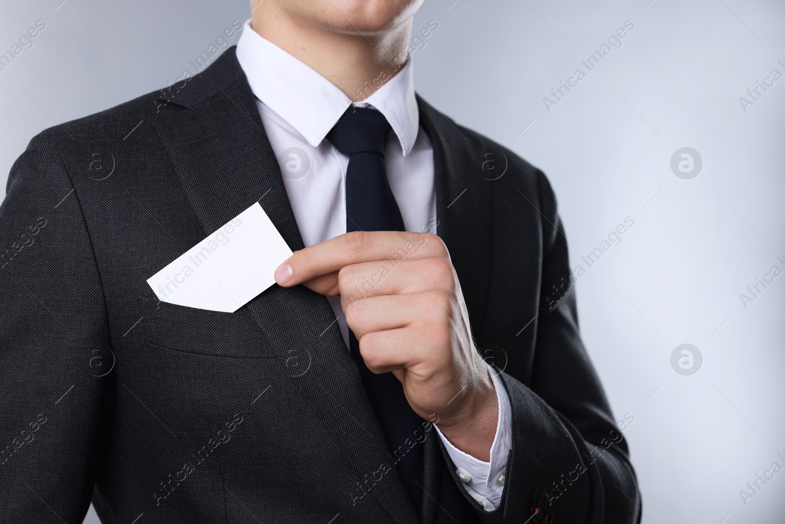 Photo of Man taking blank business card from pocket of his jacket on grey background, closeup. Mockup for design