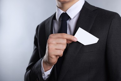 Man taking blank business card from pocket of his jacket on grey background, closeup. Mockup for design