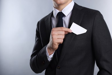 Man taking blank business card from pocket of his jacket on grey background, closeup. Mockup for design