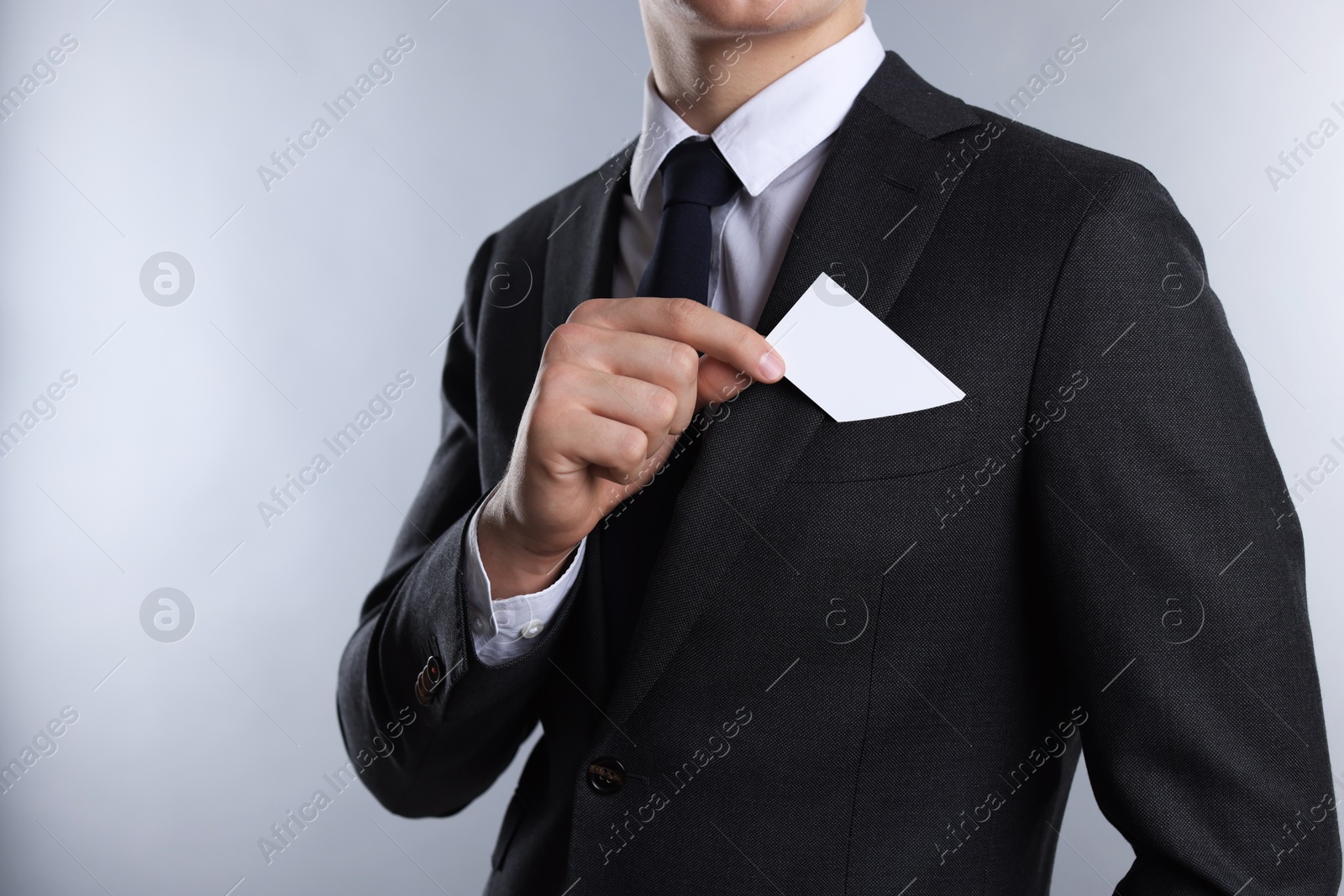 Photo of Man taking blank business card from pocket of his jacket on grey background, closeup. Mockup for design