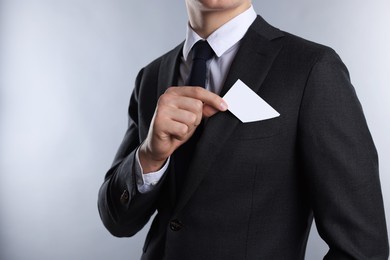 Man taking blank business card from pocket of his jacket on grey background, closeup. Mockup for design