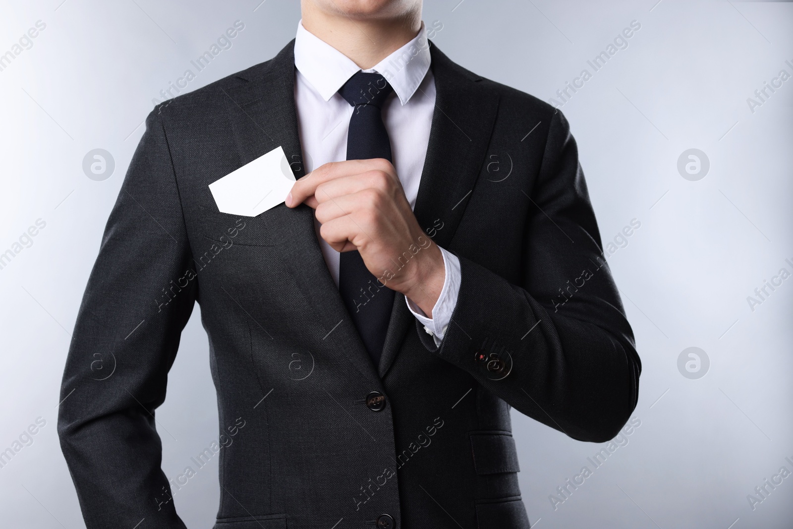 Photo of Man taking blank business card from pocket of his jacket on grey background, closeup. Mockup for design