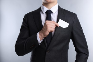 Man taking blank business card from pocket of his jacket on grey background, closeup. Mockup for design