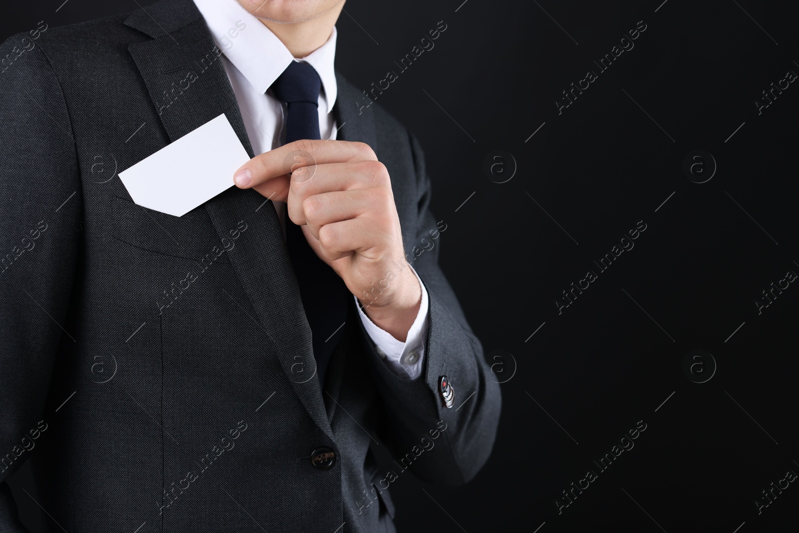 Photo of Man taking blank business card from pocket of his jacket on black background, closeup. Mockup for design