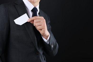 Man taking blank business card from pocket of his jacket on black background, closeup. Mockup for design