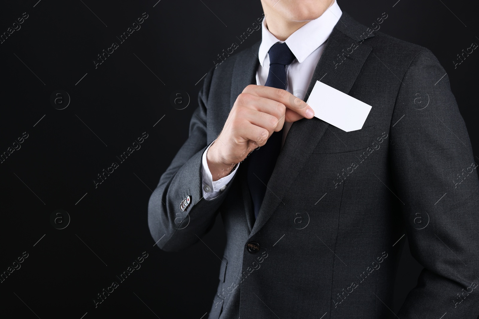 Photo of Man taking blank business card from pocket of his jacket on black background, closeup. Mockup for design