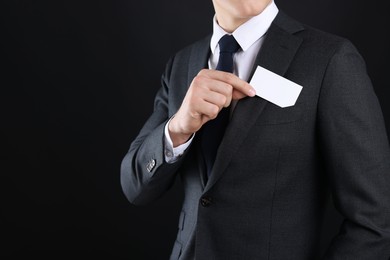 Man taking blank business card from pocket of his jacket on black background, closeup. Mockup for design