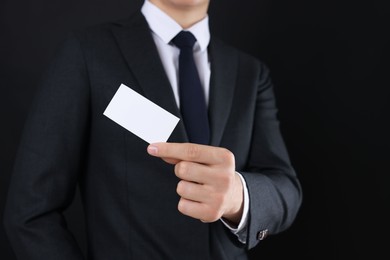 Man holding blank business card on black background, closeup. Mockup for design