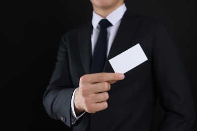 Photo of Man holding blank business card on black background, closeup. Mockup for design