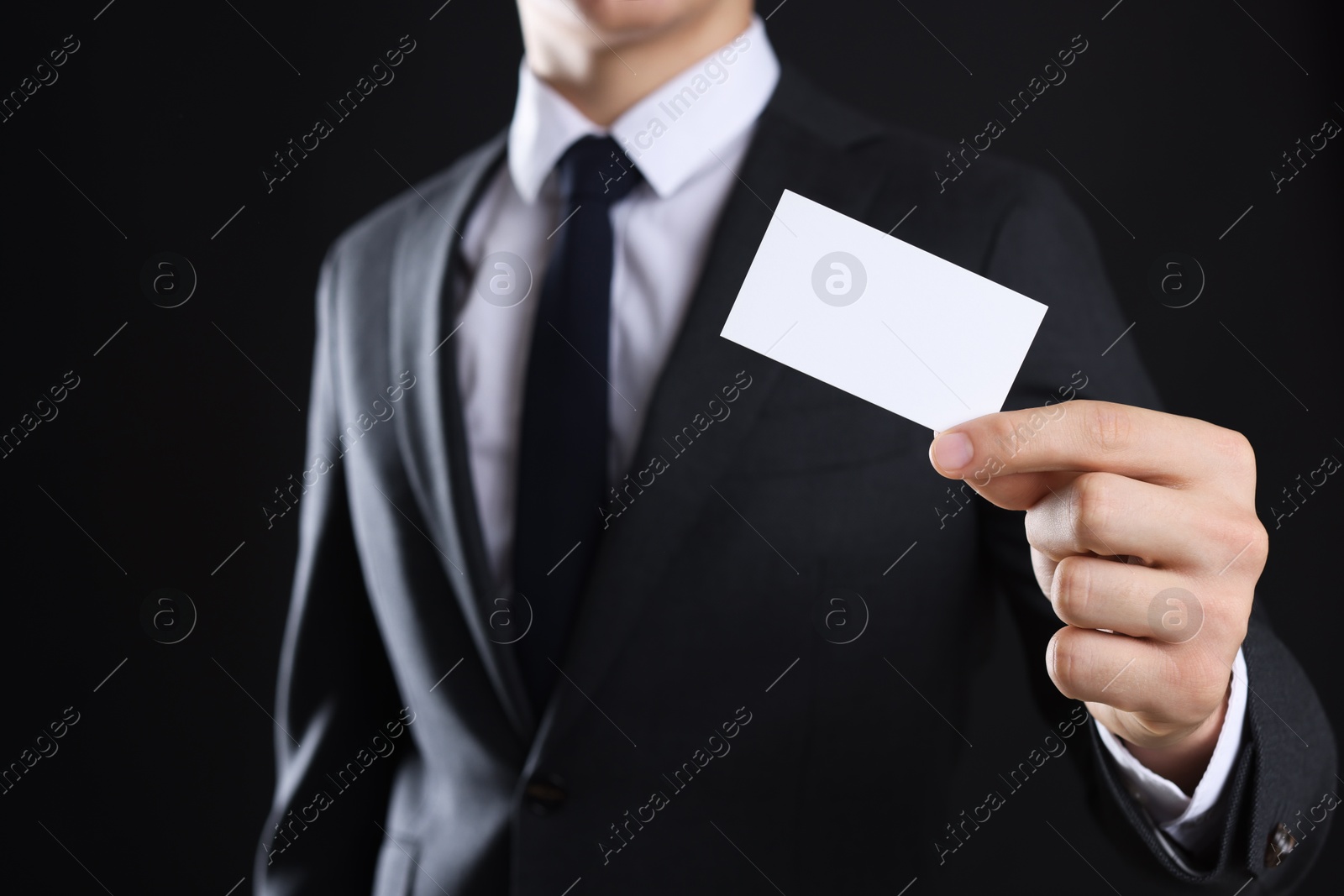 Photo of Man holding blank business card on black background, closeup. Mockup for design