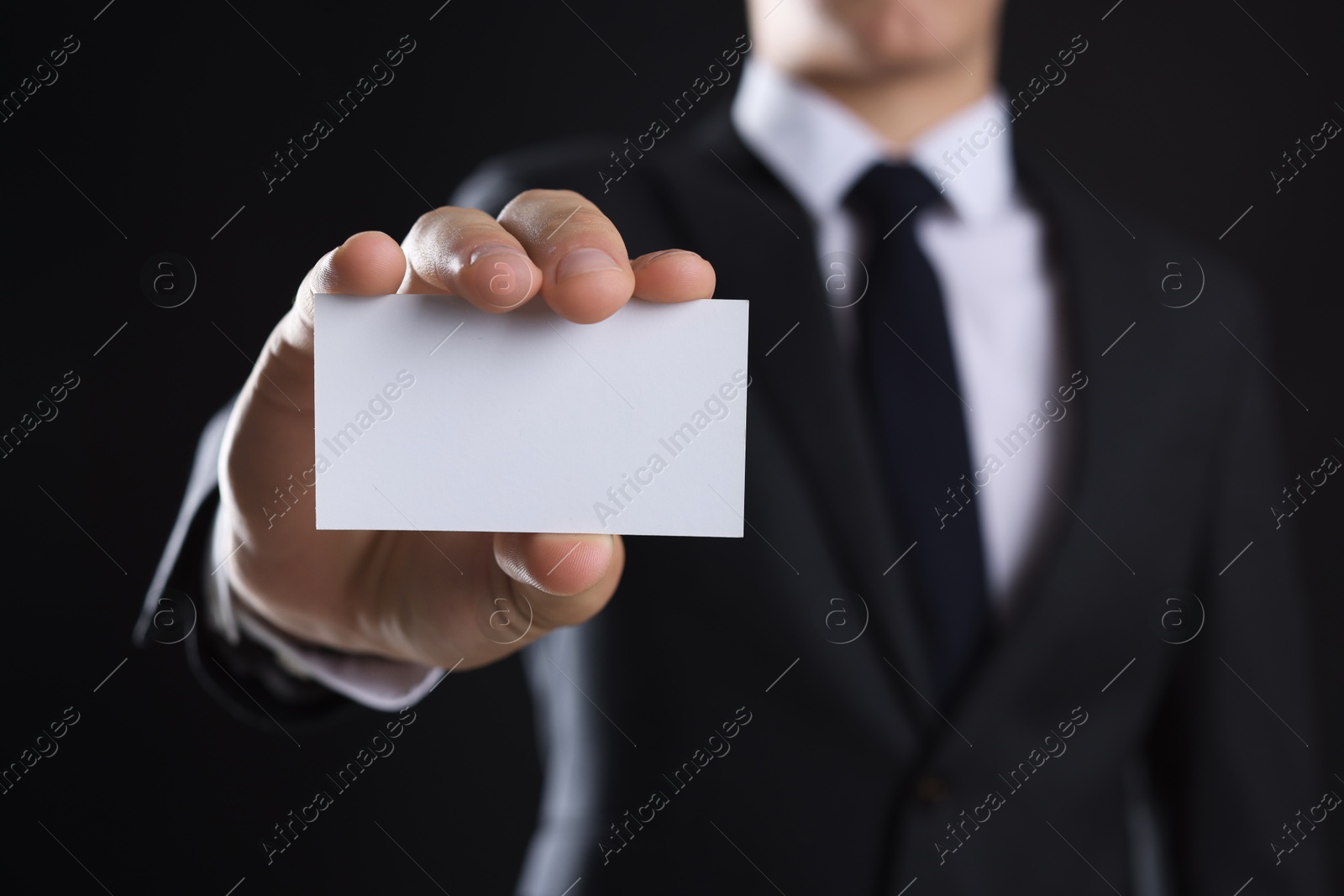 Photo of Man holding blank business card on black background, closeup. Mockup for design