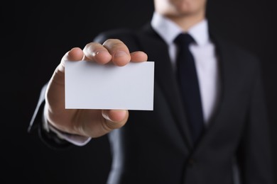 Photo of Man holding blank business card on black background, closeup. Mockup for design