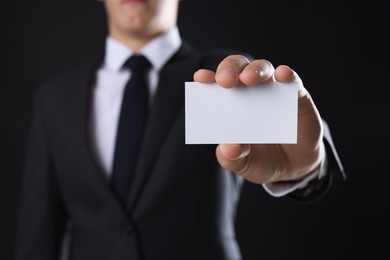 Photo of Man holding blank business card on black background, closeup. Mockup for design