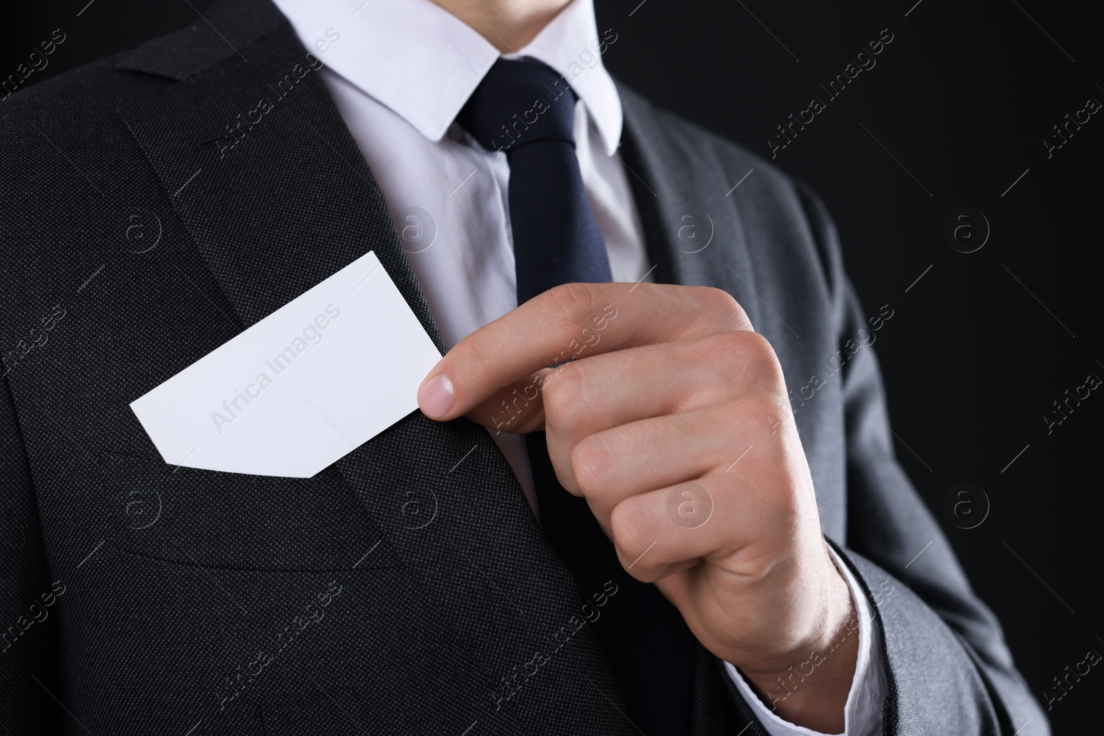 Photo of Man taking blank business card from pocket of his jacket on black background, closeup. Mockup for design