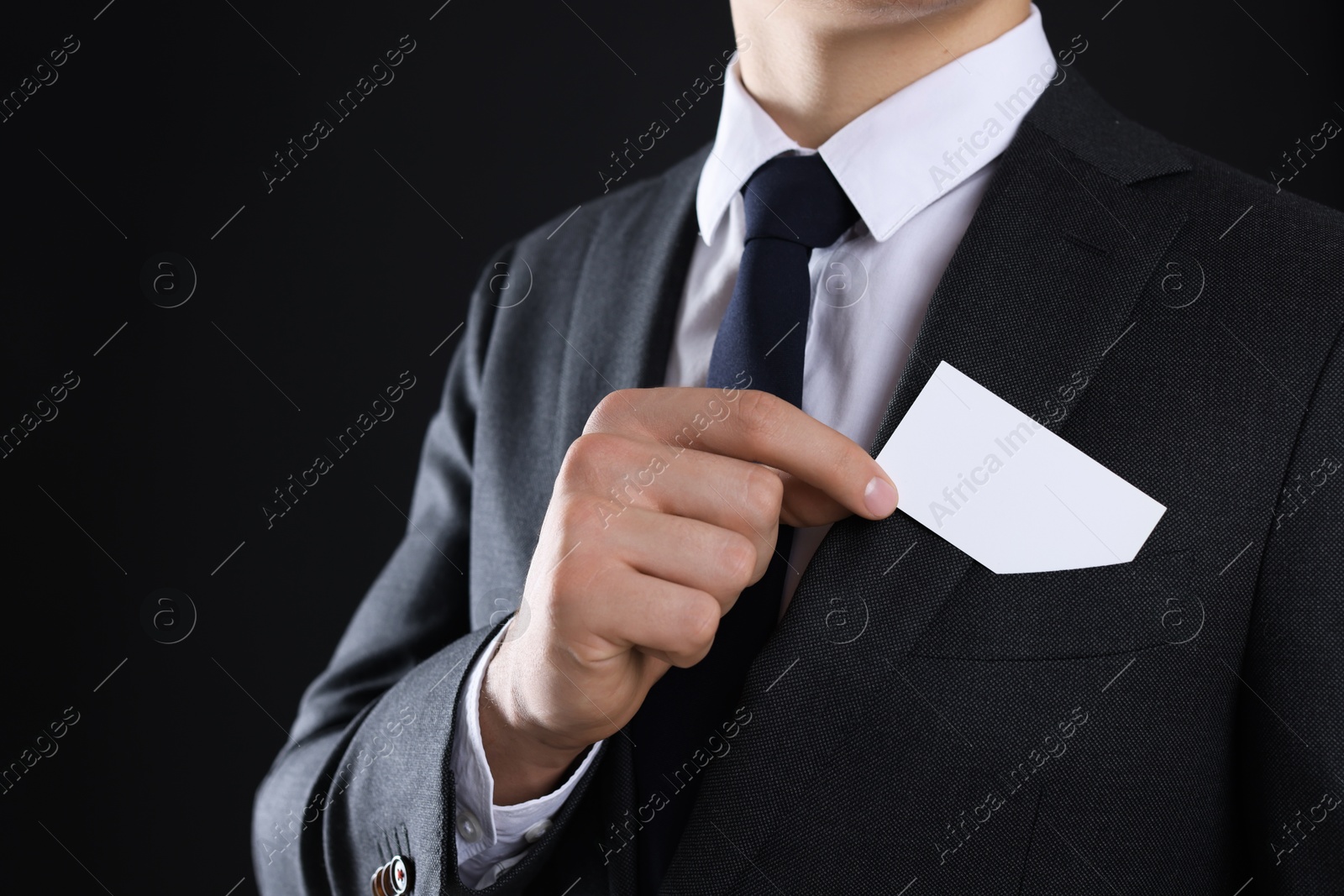 Photo of Man taking blank business card from pocket of his jacket on black background, closeup. Mockup for design