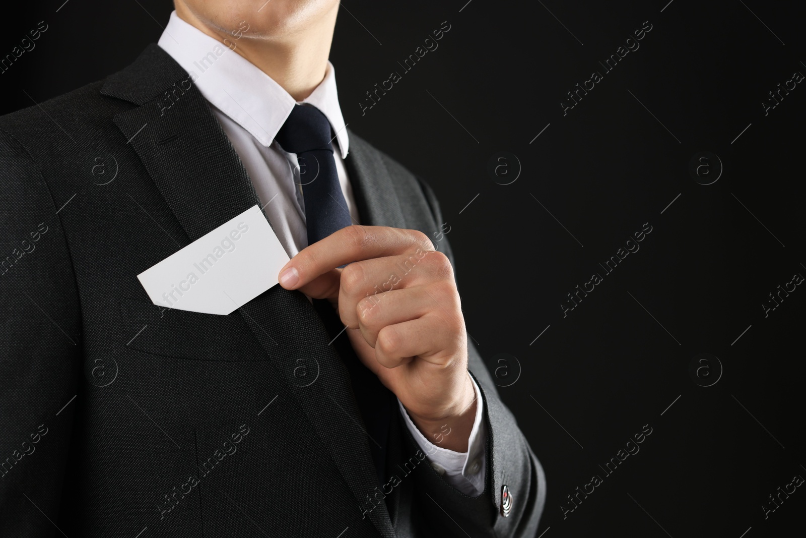 Photo of Man taking blank business card from pocket of his jacket on black background, closeup. Mockup for design