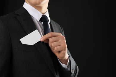 Man taking blank business card from pocket of his jacket on black background, closeup. Mockup for design